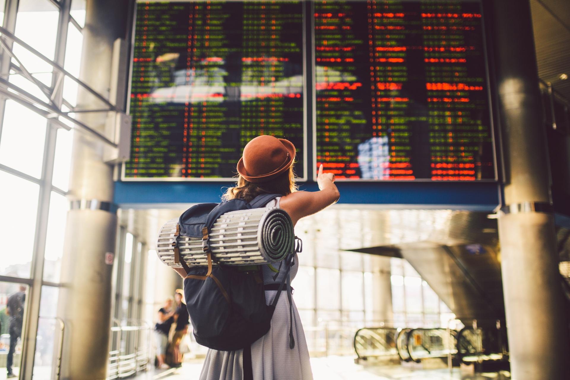 Studentin mit Rucksack zeigt auf Abflugtafel | Ghostwriter Hausarbeit